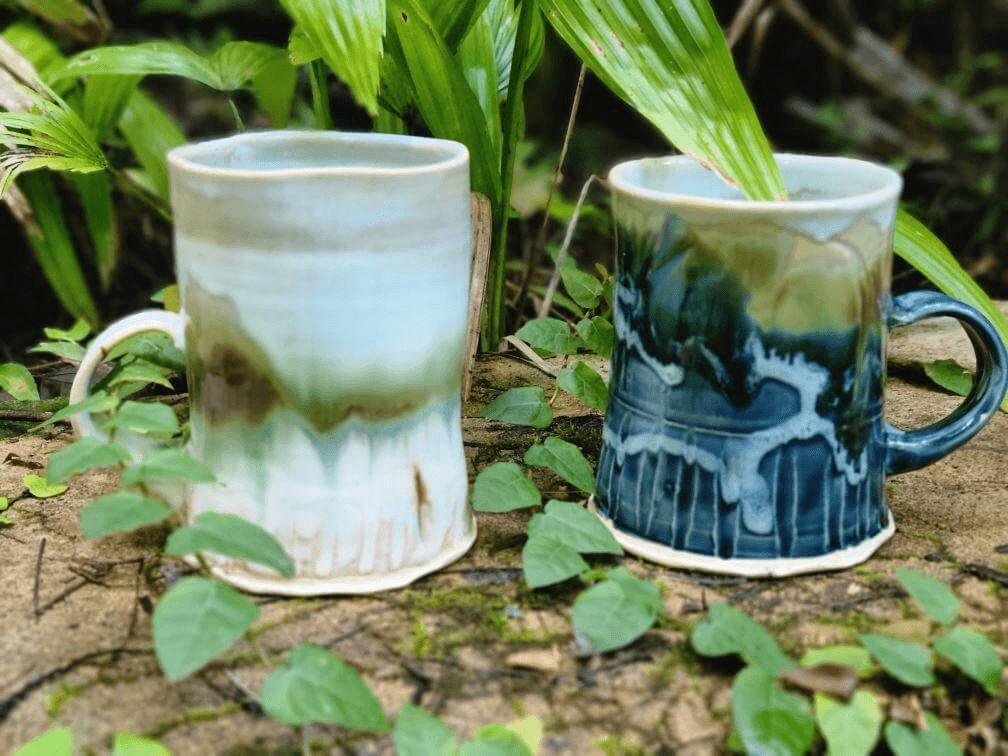 two handmade blue and white stein mugs made in Kailua, Oahu, sitting on a background of lush greenery