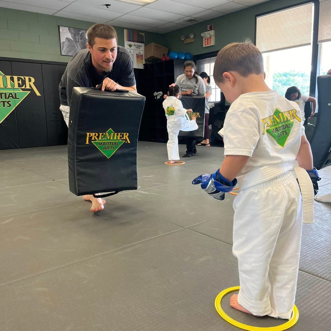A group of children are practicing karate with a teacher in a gym.