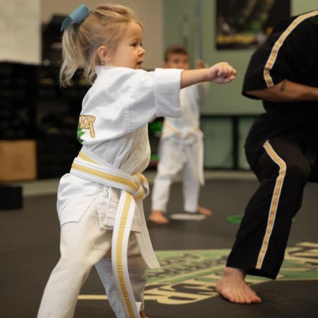 A man is kneeling down next to a young boy in a taekwondo class.