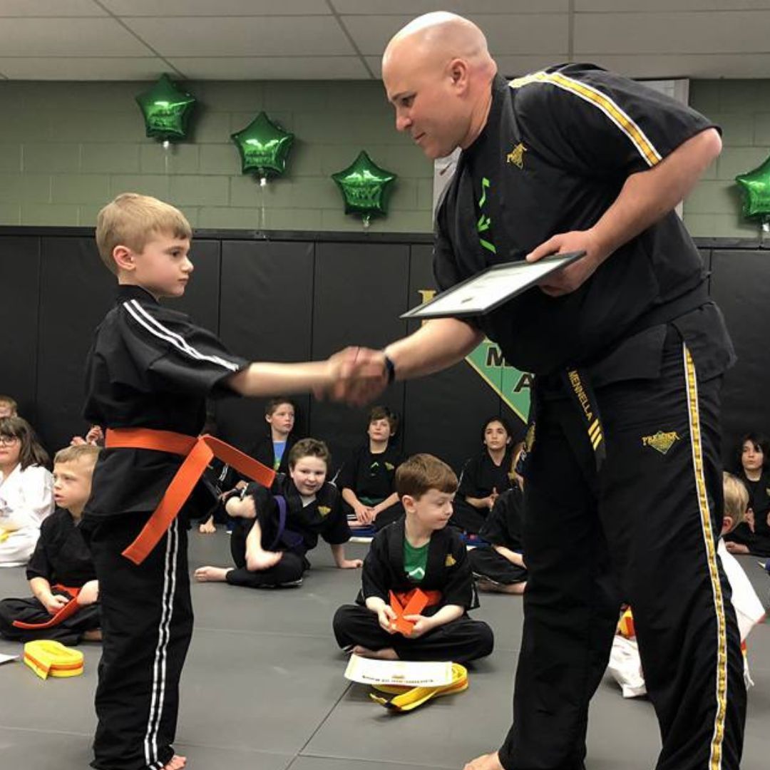 A man is kneeling down next to a young boy in a taekwondo class.