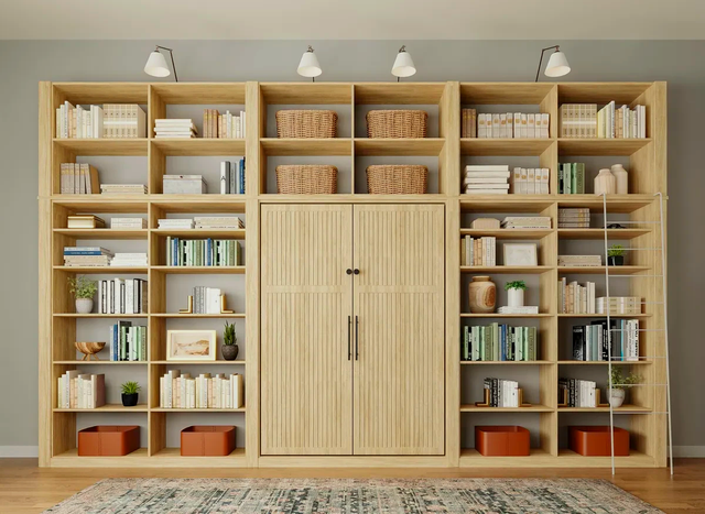 Wooden bookcase with a fold-down bed in the center, flanked by shelves of books, baskets, and decor, with lighting above.