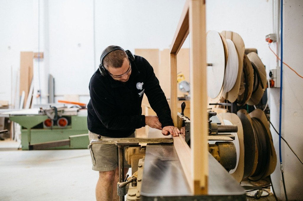 Carpenter working on a wooden frame in a workshop, wearing earmuffs.
