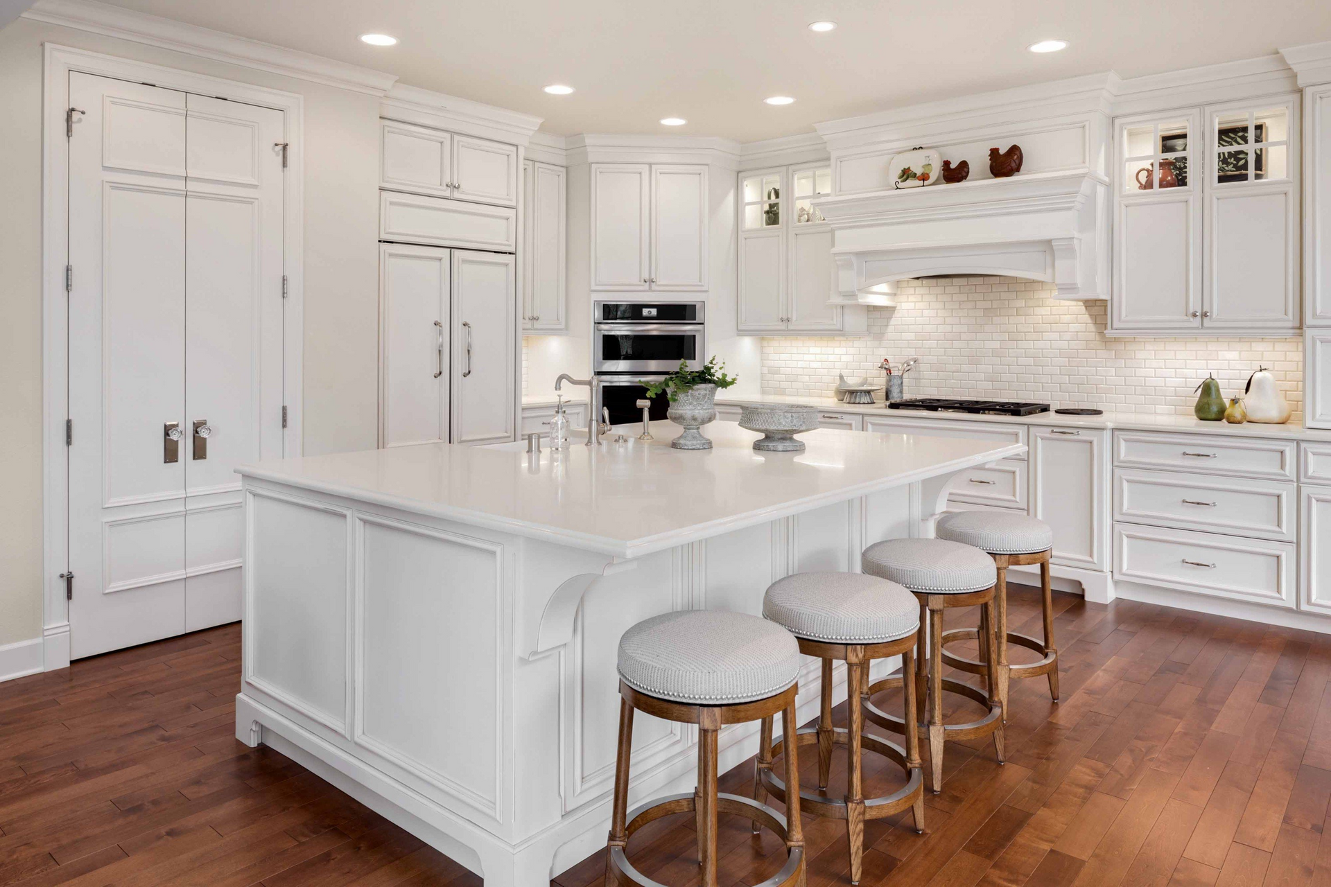 White kitchen with large island, stools, stainless steel appliances, and wood floors.