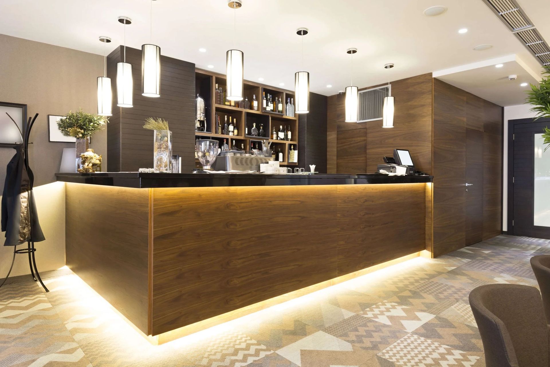 Modern hotel reception desk with warm wood paneling, pendant lights, and a patterned floor.