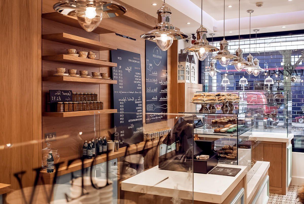 Cozy café interior with pendant lights, wooden shelves, chalkboard menus, and pastry display case.