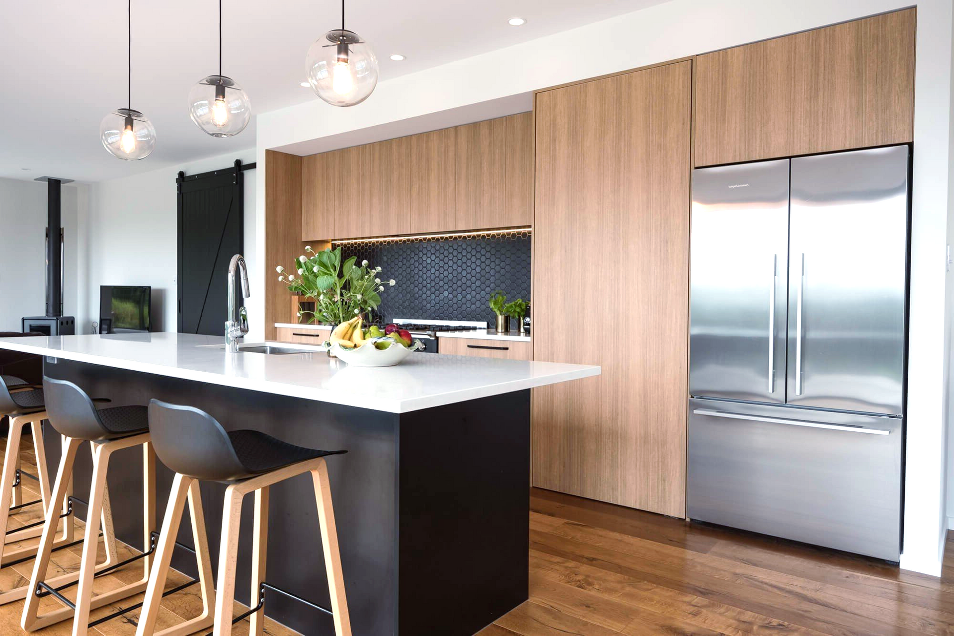 Modern kitchen with wood cabinets, stainless steel fridge, island with bar stools, and globe pendant lights.