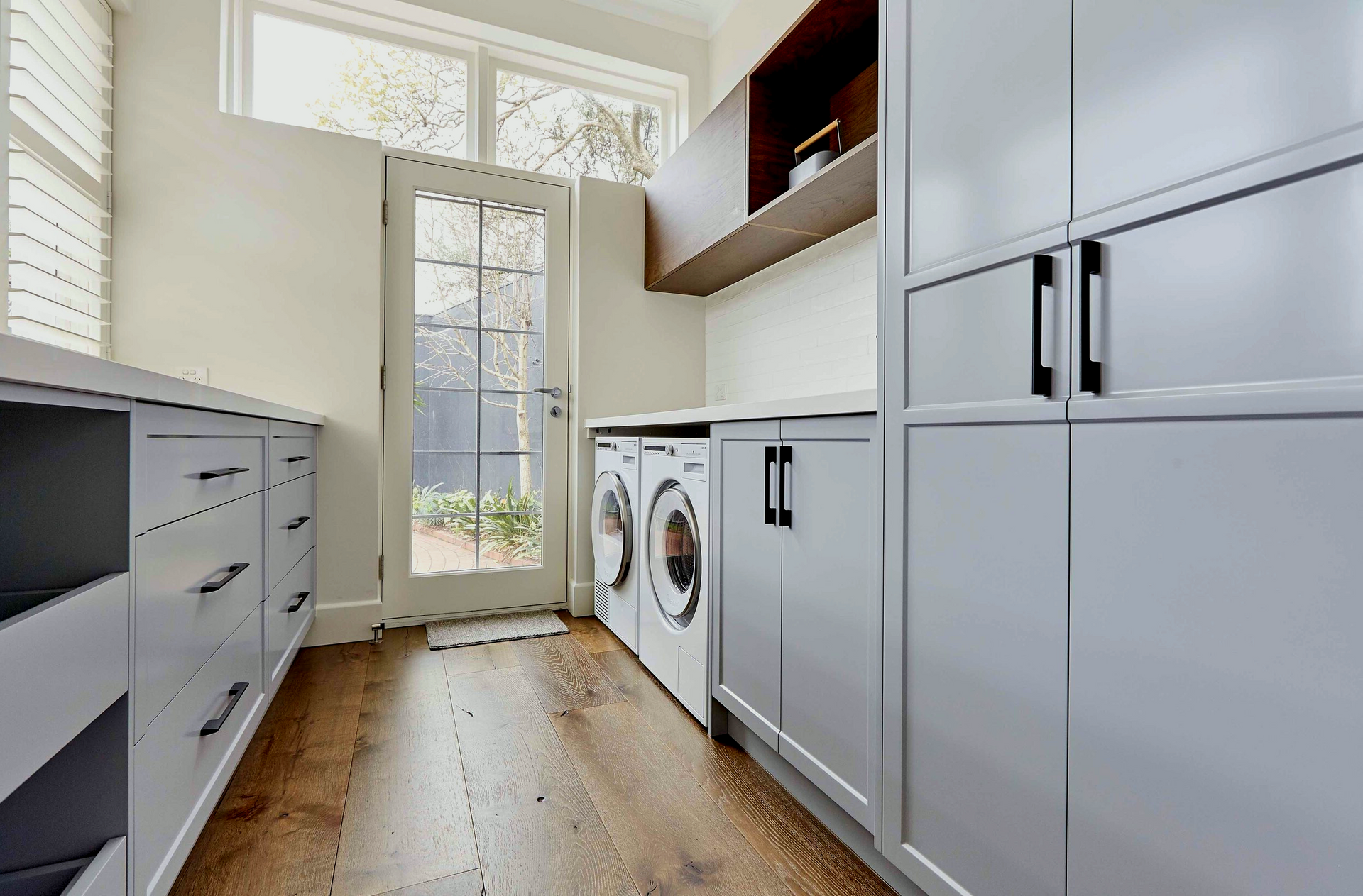 Laundry room with gray cabinets, wooden floors, and a doorway to a yard.