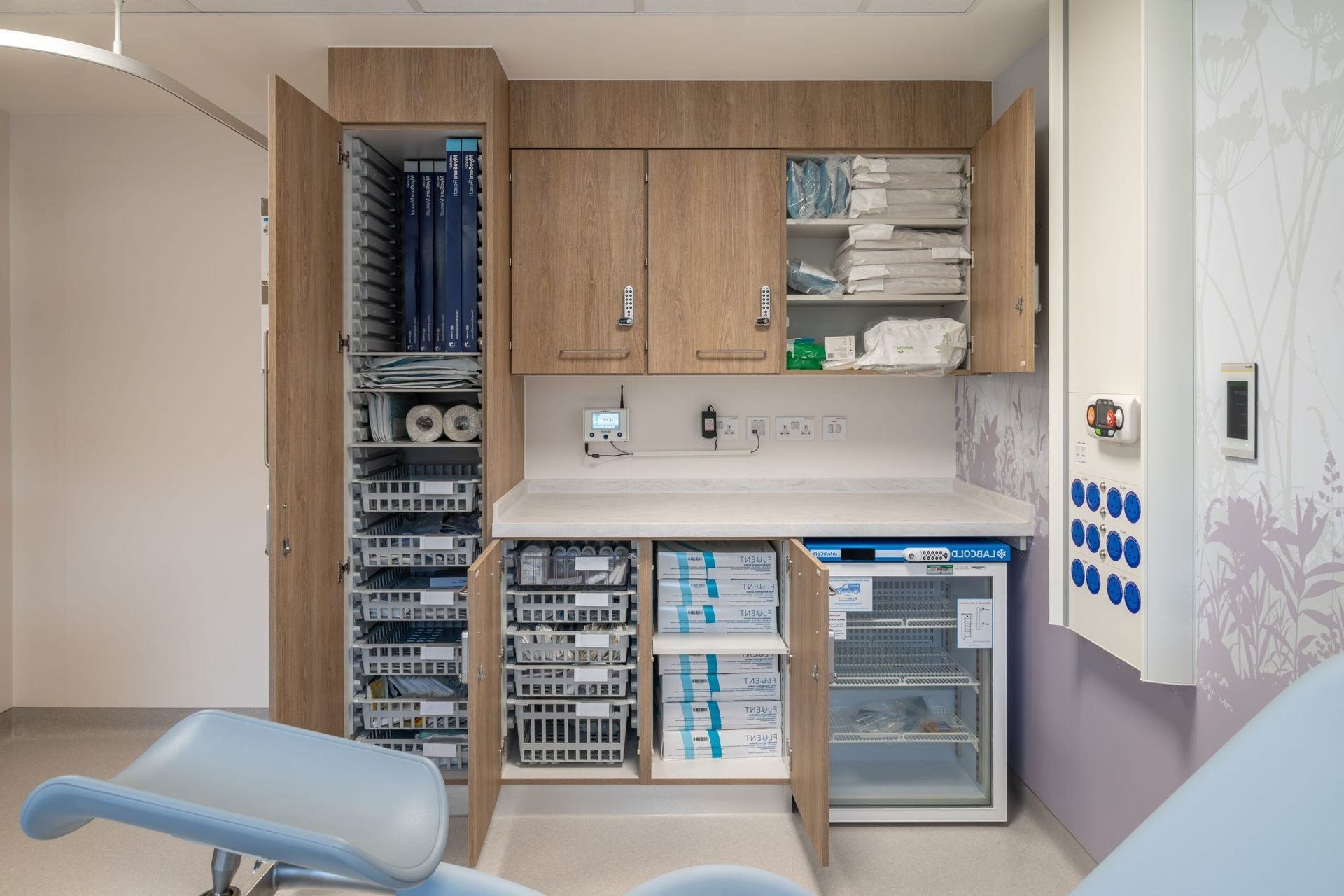 Dentist treatment room with cabinets, sterilisation equipment, and a blue dental chair.