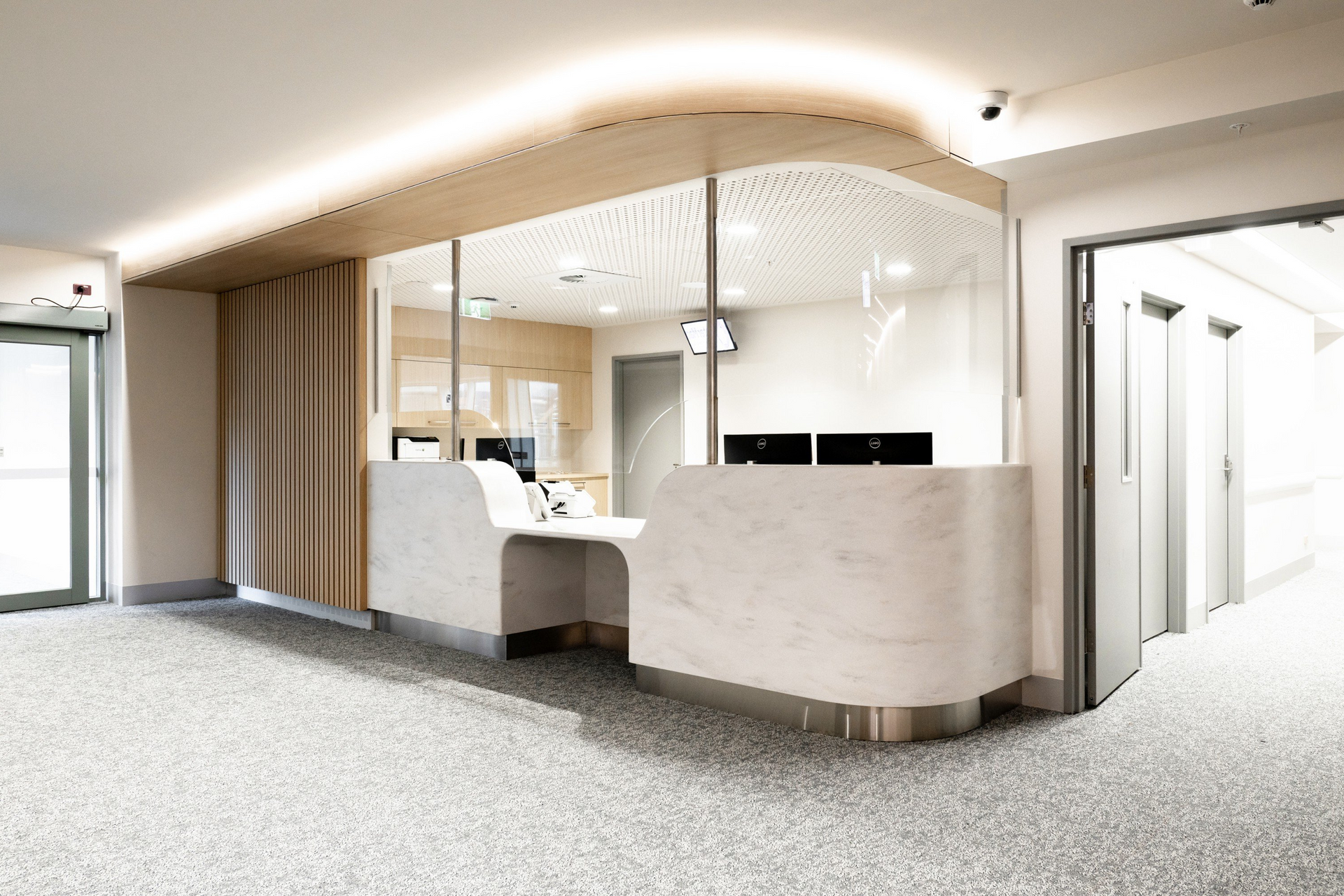 Modern office lobby with curved reception desk, wood-paneled walls, and bright glass partitions