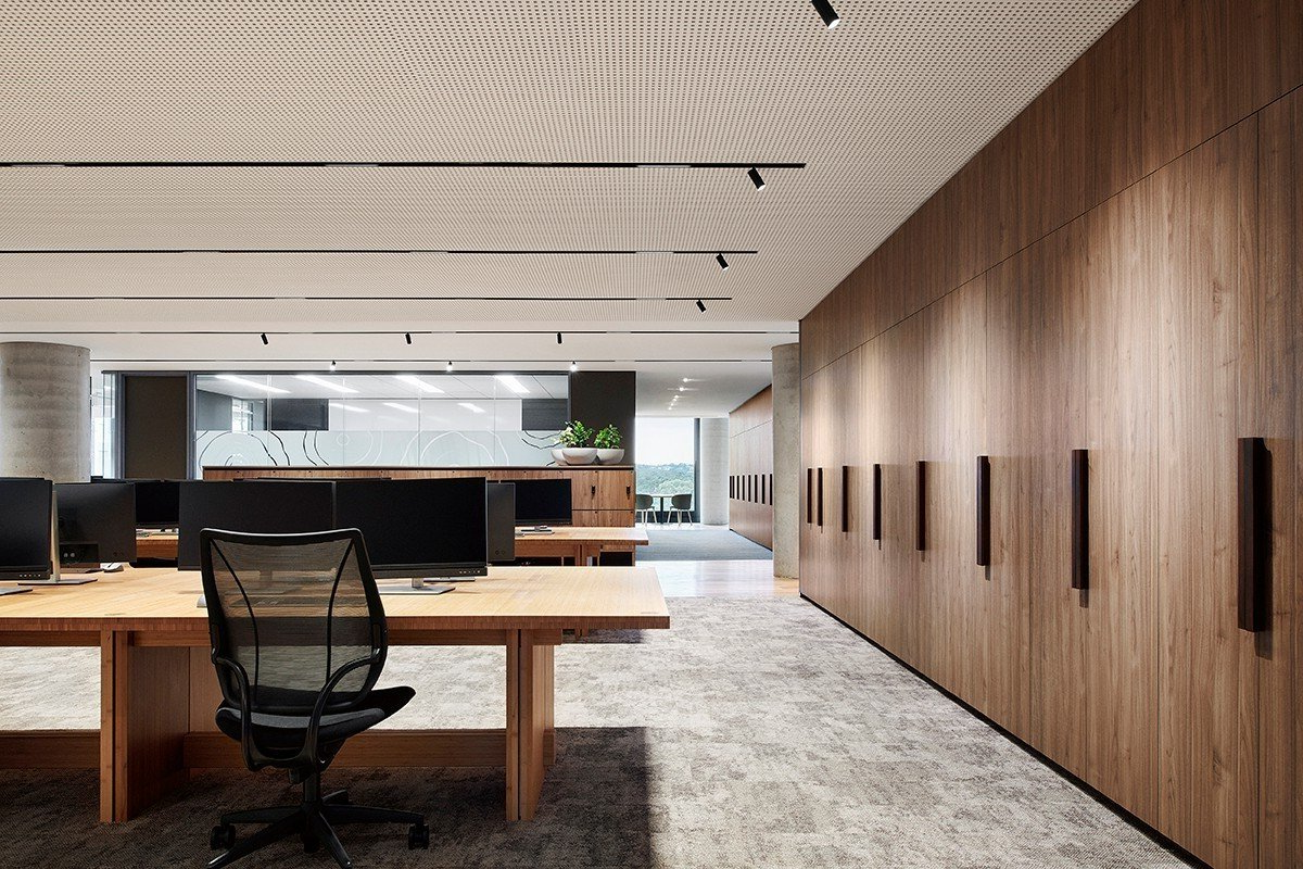 Modern office interior with wooden desks, black chairs, and a wood-paneled wall with framed art.