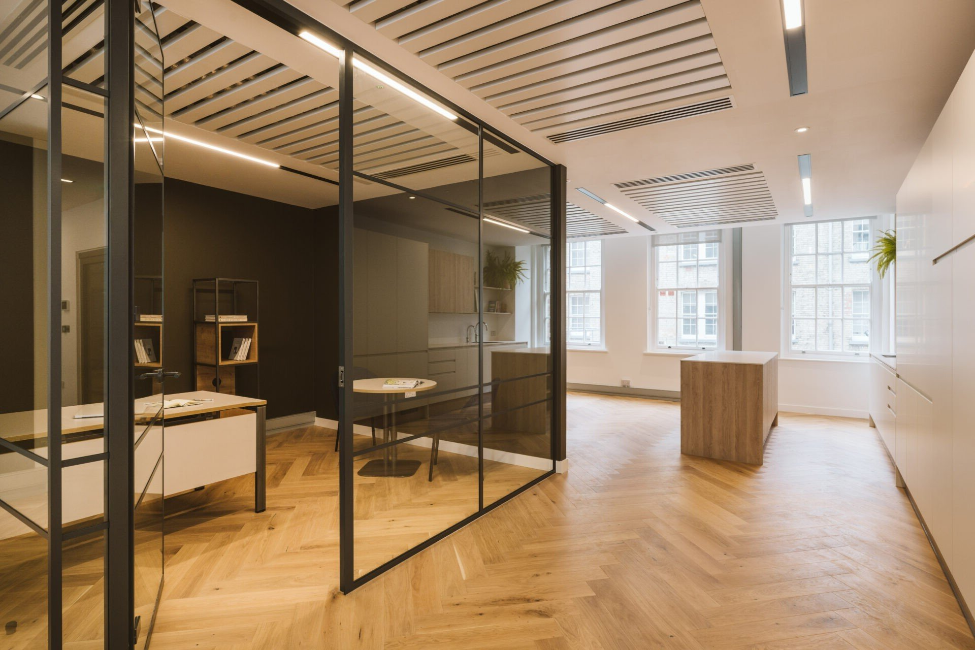 Modern office with glass-walled meeting room, wood floors, desks, and bright windows.