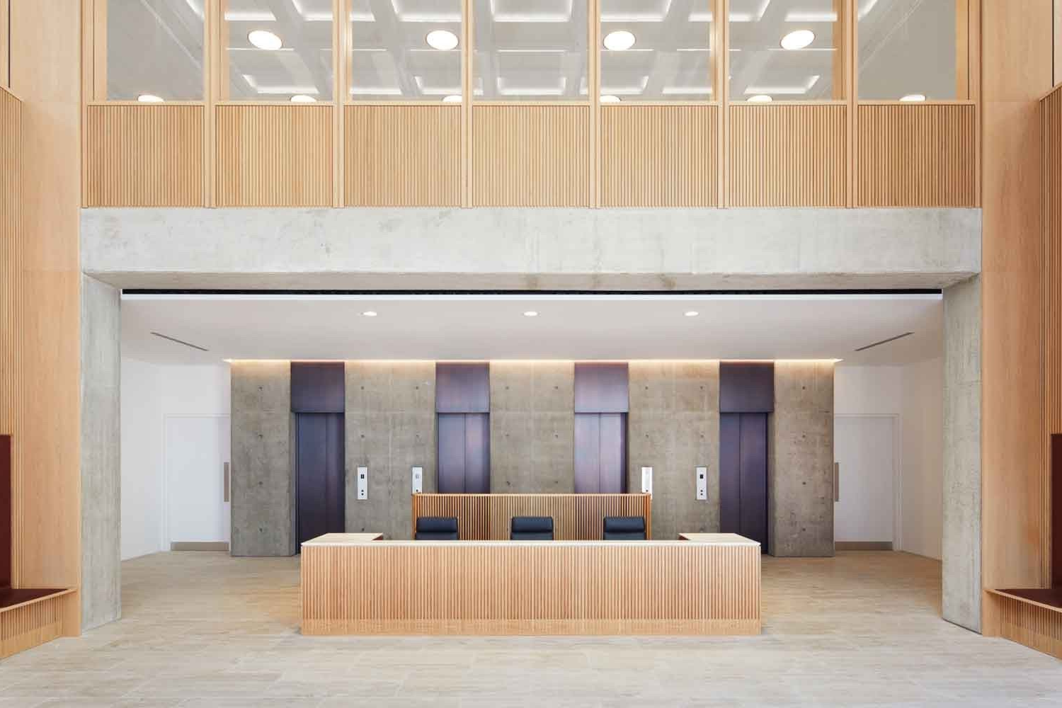 Modern lobby with wooden accents, reception desk, and elevators in a bright minimalist interior.
