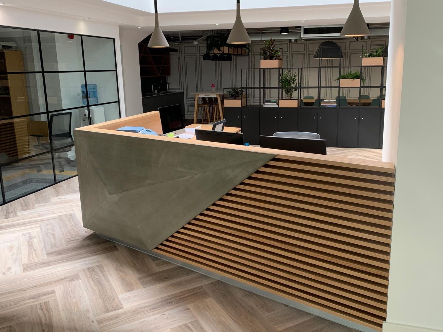Modern office reception desk with wood slats, gray paneling, and glass-walled meeting space behind.