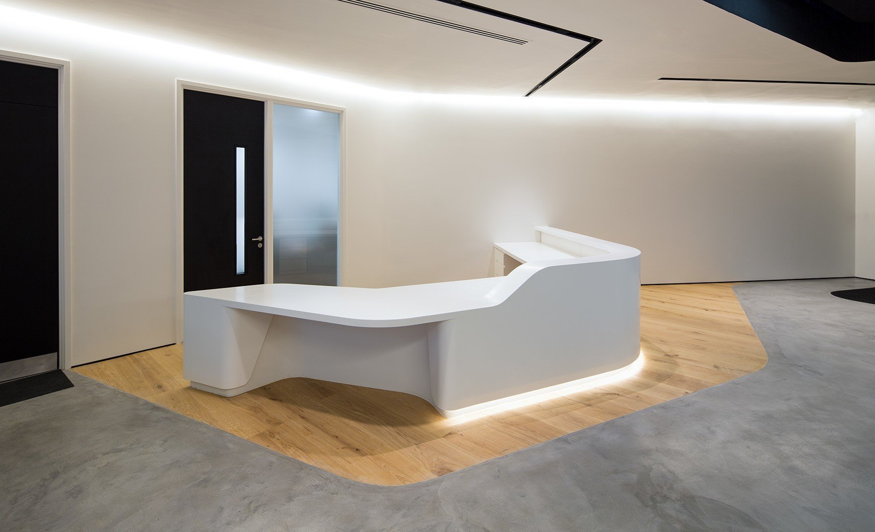 Modern office reception area with curved white desk, wood floor, and minimalist lighting