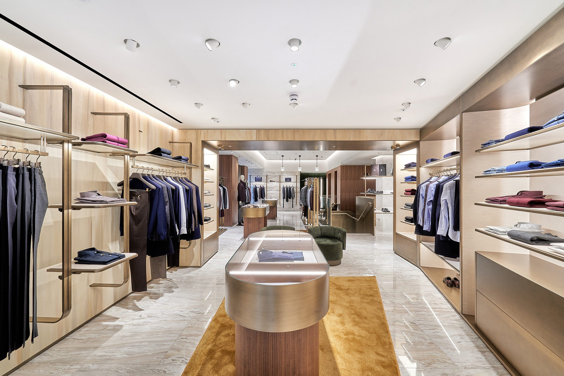 Bright clothing boutique with shelves, hanging garments, and a central display table under warm lighting.