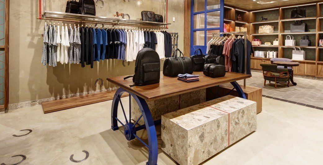 Boutique display with jeans, sweaters, backpacks, and a wooden table on a white floor.