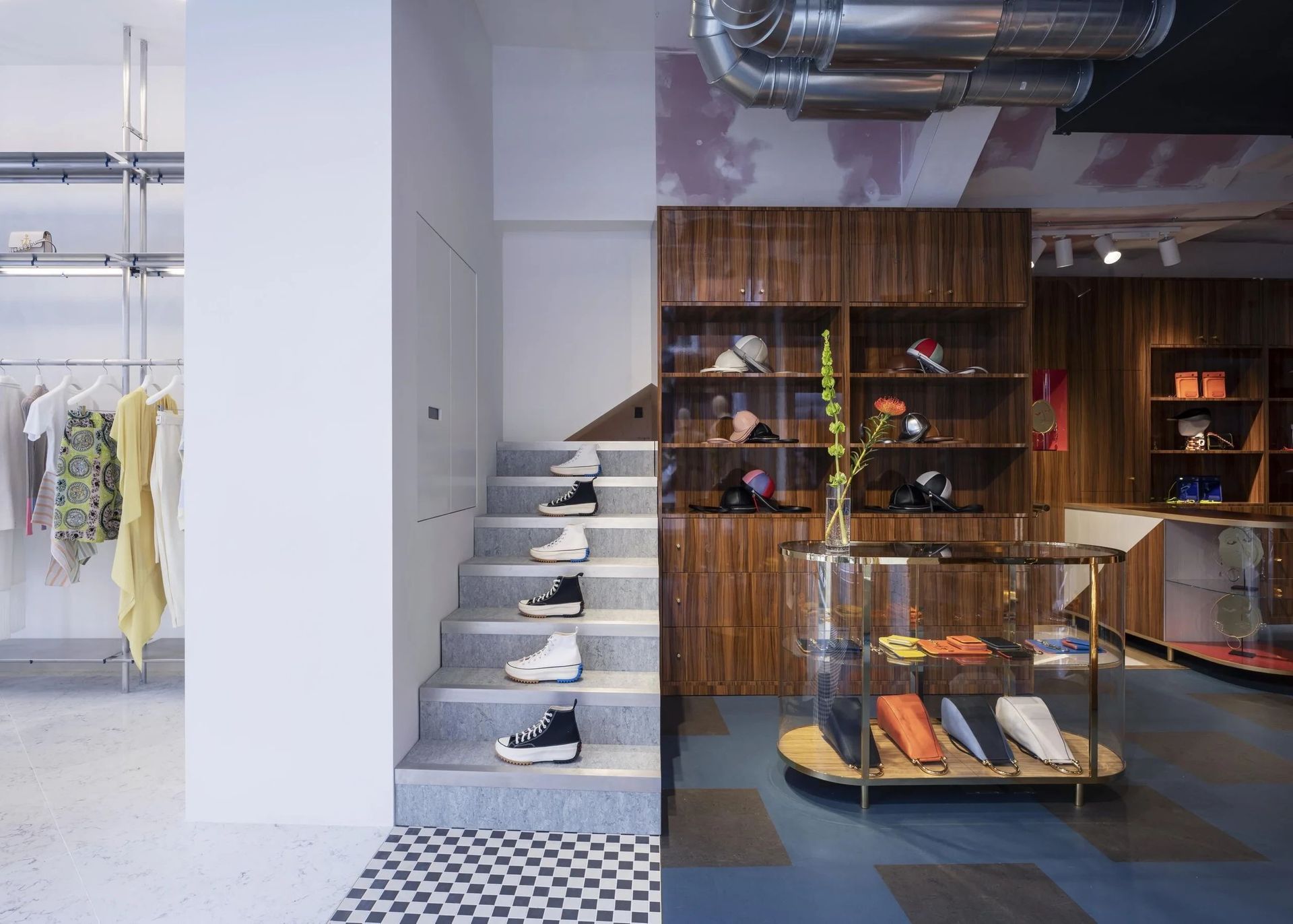 Shoe store interior with stairs, shelves of shoes, and clothing racks in a minimalist white and wood space.