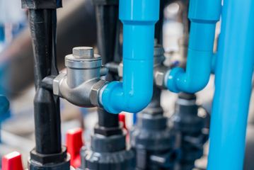 Blue and black water pipes connected to a metal valve in a plumbing system