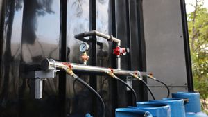 Industrial piping and valves mounted on a black tank, with hoses connected and a blue drum below