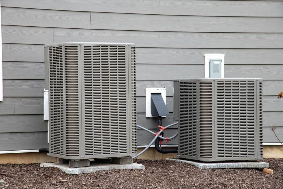 Two outdoor HVAC units beside a gray house with visible utility connections.