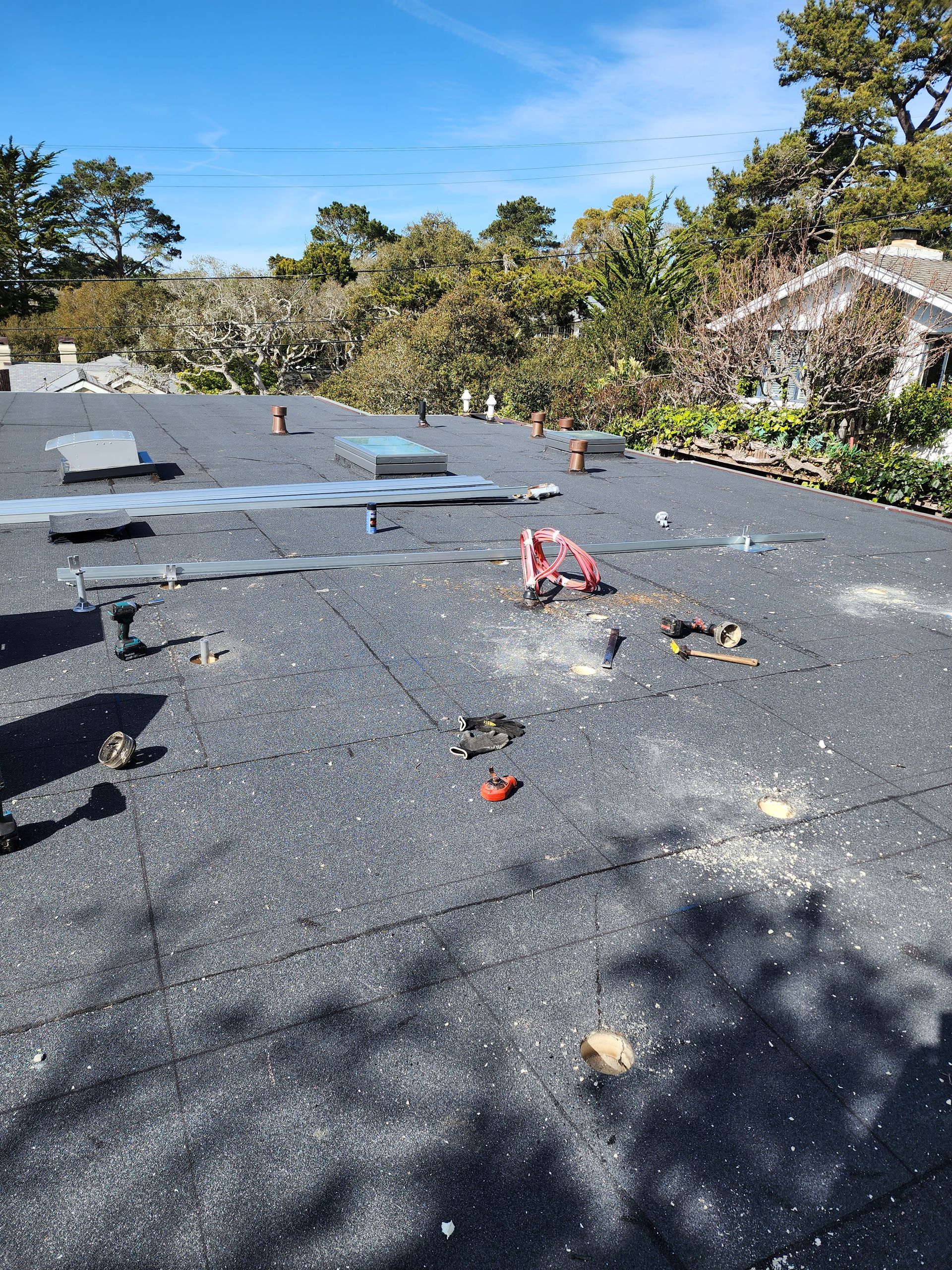 Flat roof with debris, vent pipes, and a skylight; trees and a house in the background.