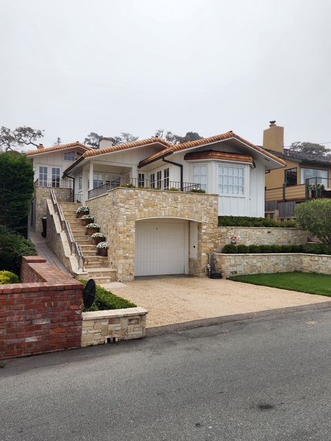 White house with tan stone facade, stairs leading to the entrance, and a garage door. Overcast day.