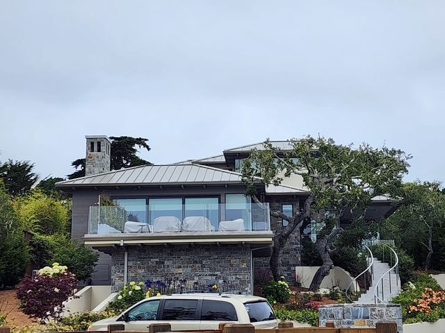 A modern home with stone facade, balcony, chimney, and gray roof, under a cloudy sky.