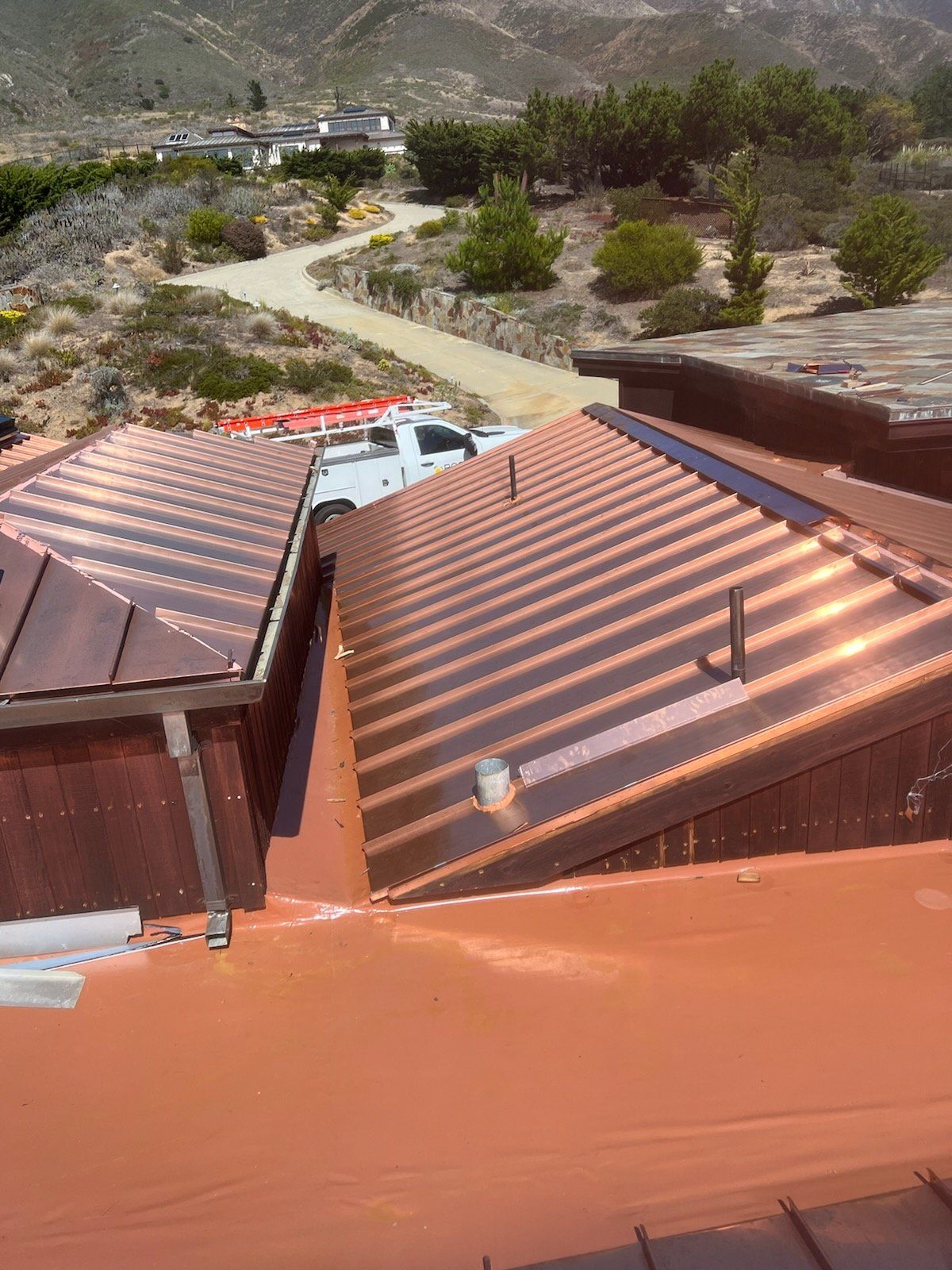 Copper-colored metal roofs on a building, with a white truck parked nearby, in a sunny outdoor setting.