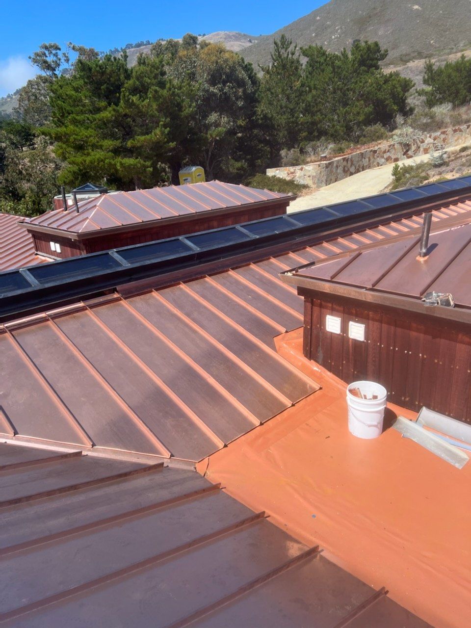Copper roof with dark solar panels, white bucket, and mountain backdrop.