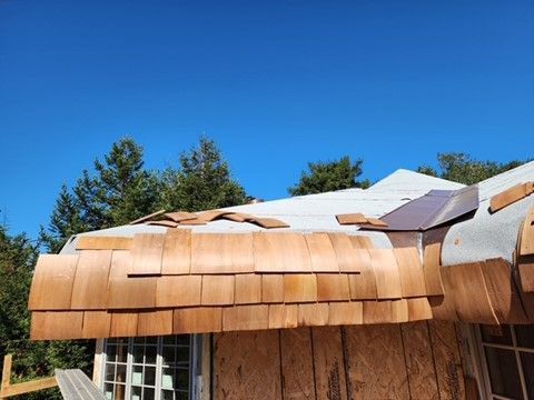 Cedar shingles being installed on a roof with a blue sky background.