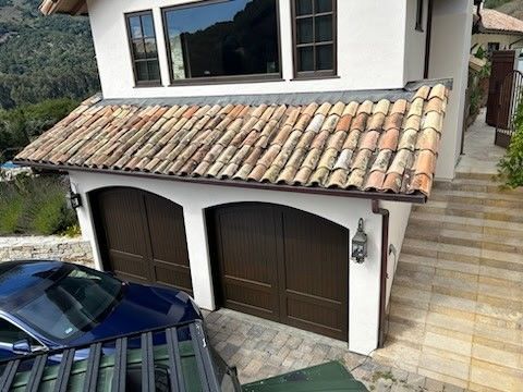 Two-car garage with brown doors, terracotta tile roof, and a blue car parked in front.