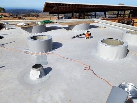 Rooftop construction: Gray flat roof with several circular structures, a leaf blower, and orange extension cord.