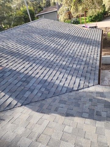 Overhead view of a newly shingled roof, varying shades of gray, under a sunny sky.