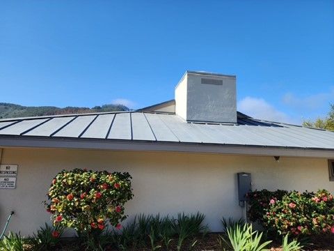 Building with gray metal roof, white walls, and a large vent. Blue sky.