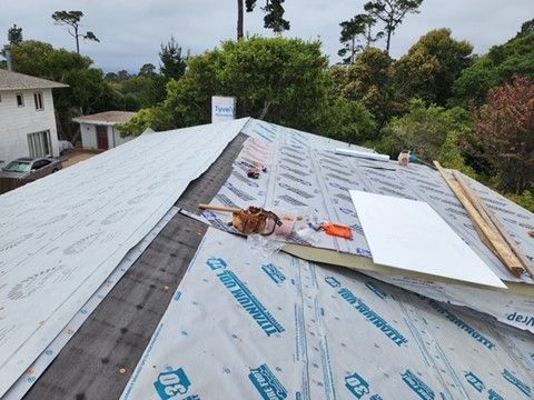 Rooftop with Tyvek wrap, construction materials, and trees in background.