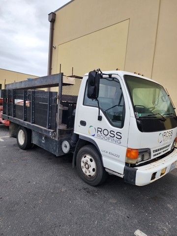 White Ross Roofing truck parked in front of a building; black bed with metal framing.