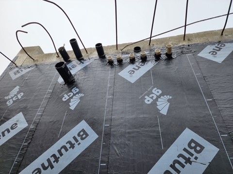 Black waterproof membrane with pipes and rebar on a building's roof. 