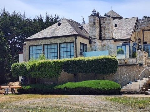 Stone house with slate roof, manicured hedges, and steps leading to a side entrance.