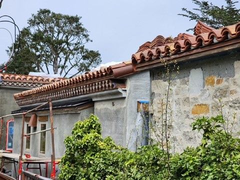 Old stone building with terracotta tile roof and foliage in front.