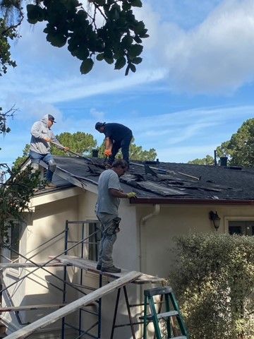 Roofers removing shingles from a house roof on a sunny day.