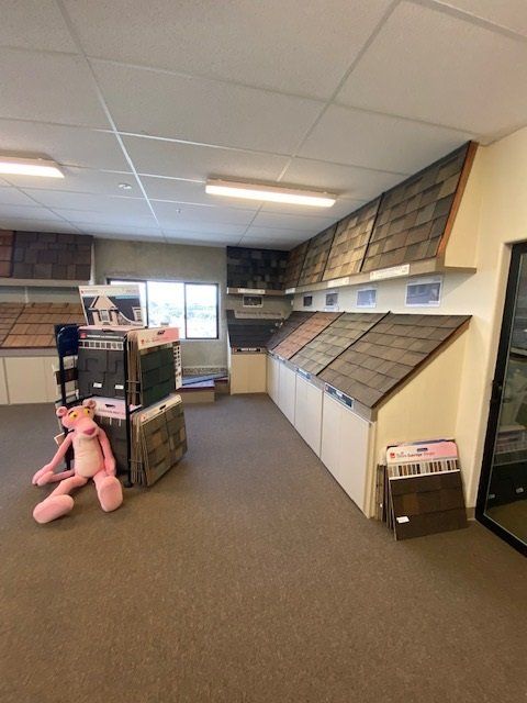 Roofing samples displayed in a showroom. A Pink Panther plush toy sits on the floor.