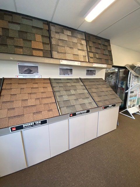 Roofing shingle samples displayed on white cabinets in a showroom; various colors and textures.