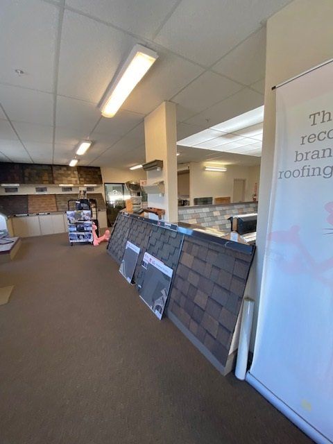 Interior of a roofing supply store displaying sample shingles. Brown carpet, fluorescent lights.