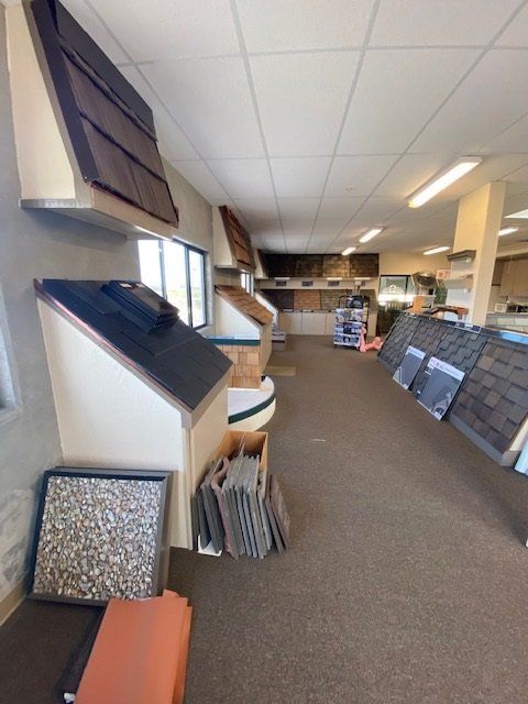 A showroom displaying various roofing materials and styles. Brown carpet, neutral walls, and overhead lighting.