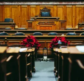 Empty wood-paneled courtroom with benches, a judge’s bench, and red poinsettias in the center aisle