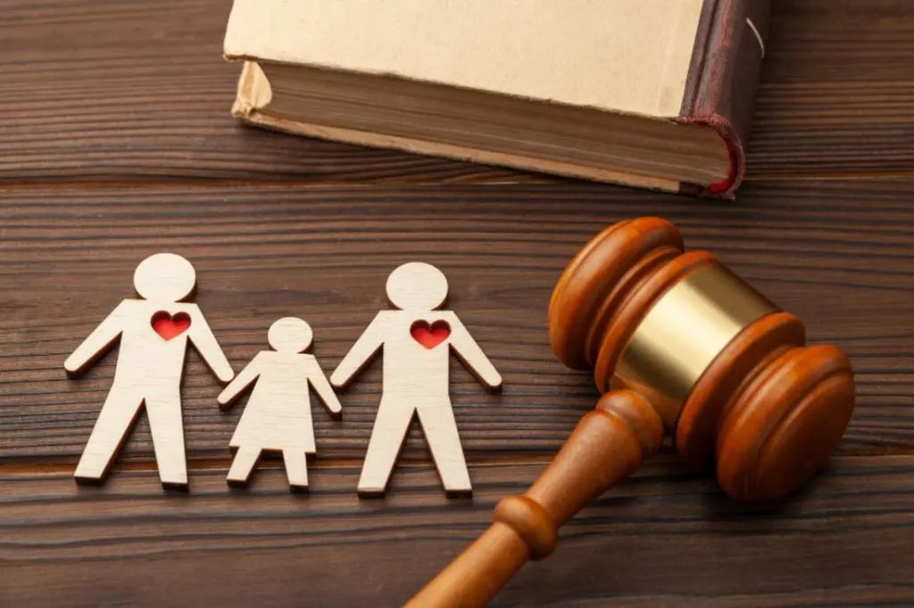 Paper family cutouts with red hearts beside a judge’s gavel and book on a wooden desk