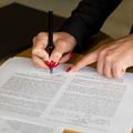 Hands signing a document with a black pen on a desk