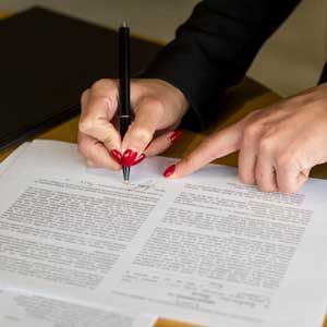 Hands signing a document with a black pen on a desk