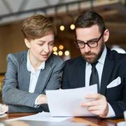 Two coworkers in business attire reviewing a document at a table in a softly lit office