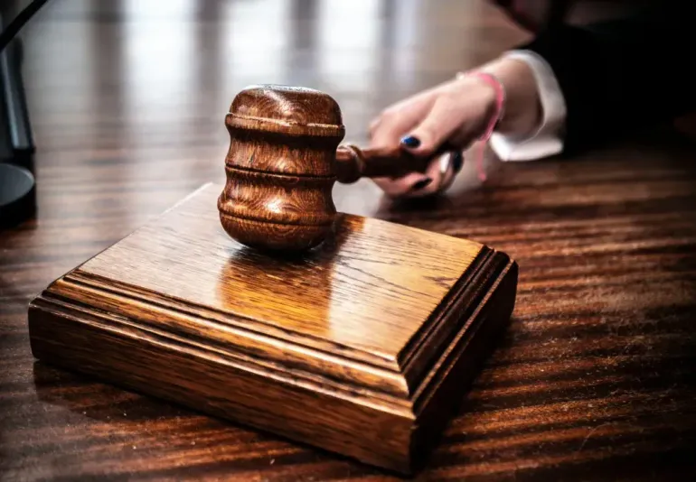 Judge’s gavel on a wooden base, with a hand in the background reaching for it